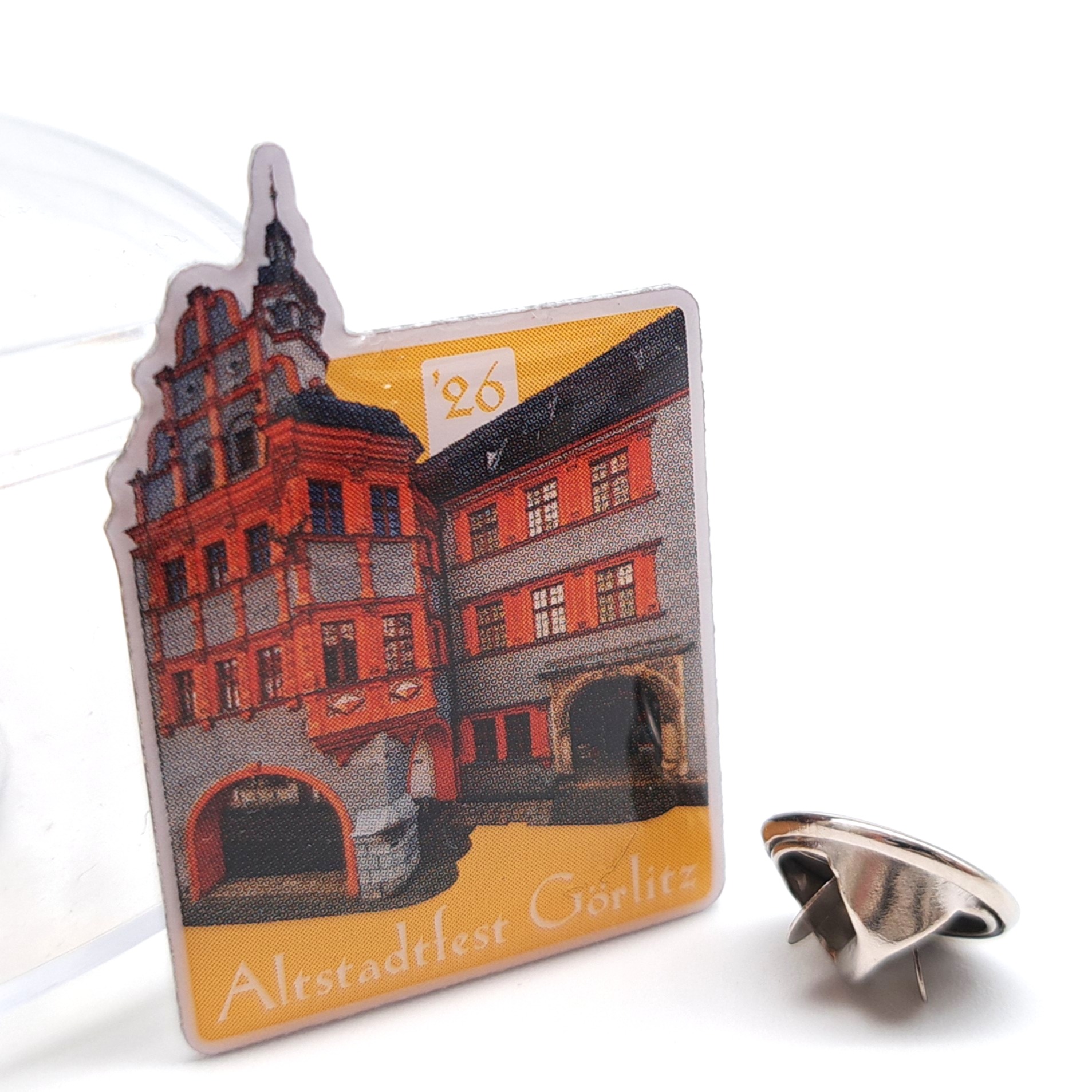 Auf der Vorderseite des Altstadtfestpins 2026 ist der Schönhof zu mit gelben Hintergrund zu sehen