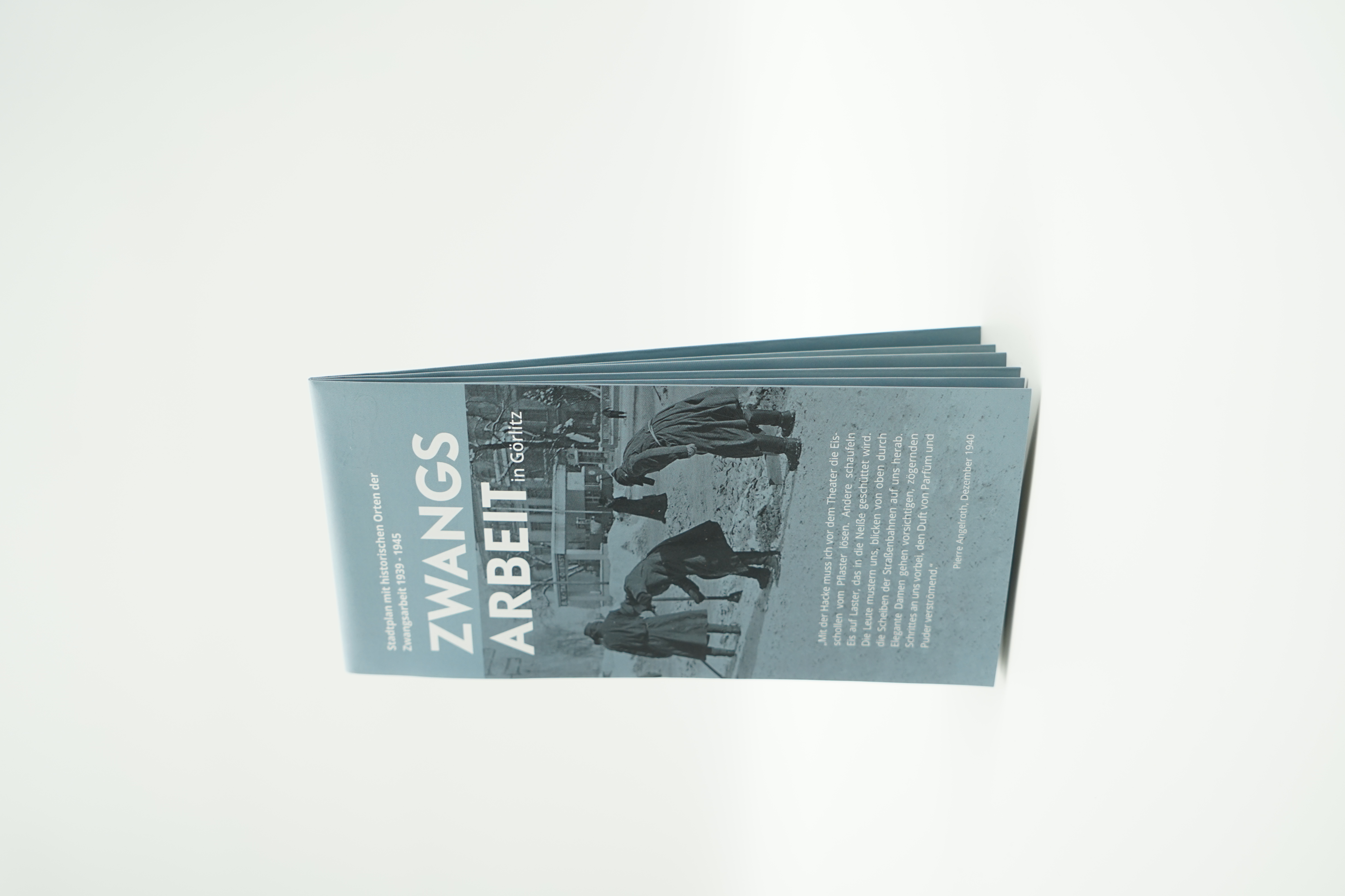 Der grau-blau gefaltete Plan zum Thema Zwangsarbeit  ist hier aufgestellt. Auf der Titelseite ist ein Foto aus der Zeit zu erkennen. Ebenso Text in weißer Schrift.
