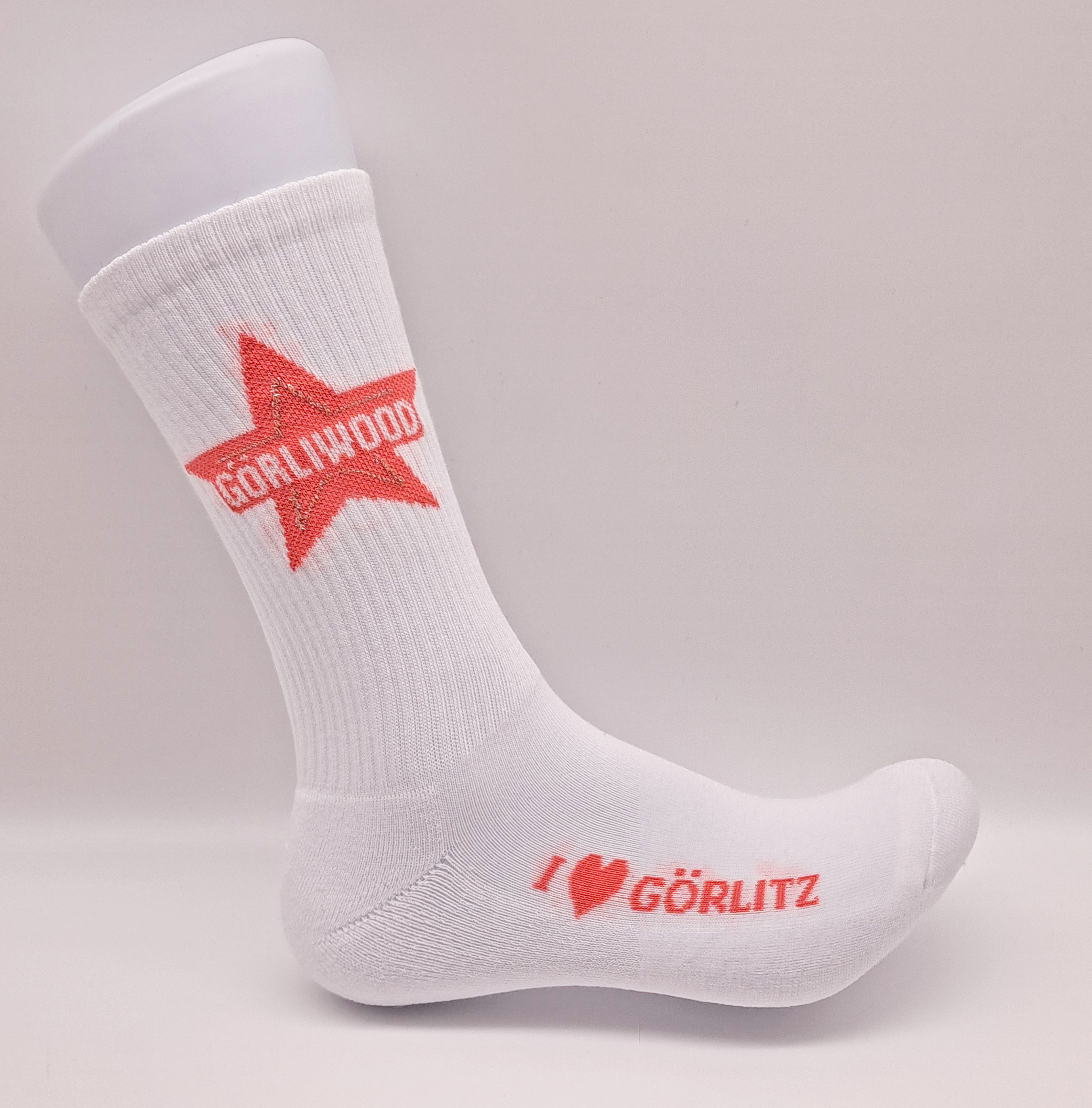 Ein weißer Dekofuss trägt eine weiße Tennissock. Am Sockenschaft ist in orange-roter Farbe der Görliwood-Stern mit der weißen Schrift GÖRLIWOOD. Seitlich am Fußspann steht I Herzsymbol Görlitz