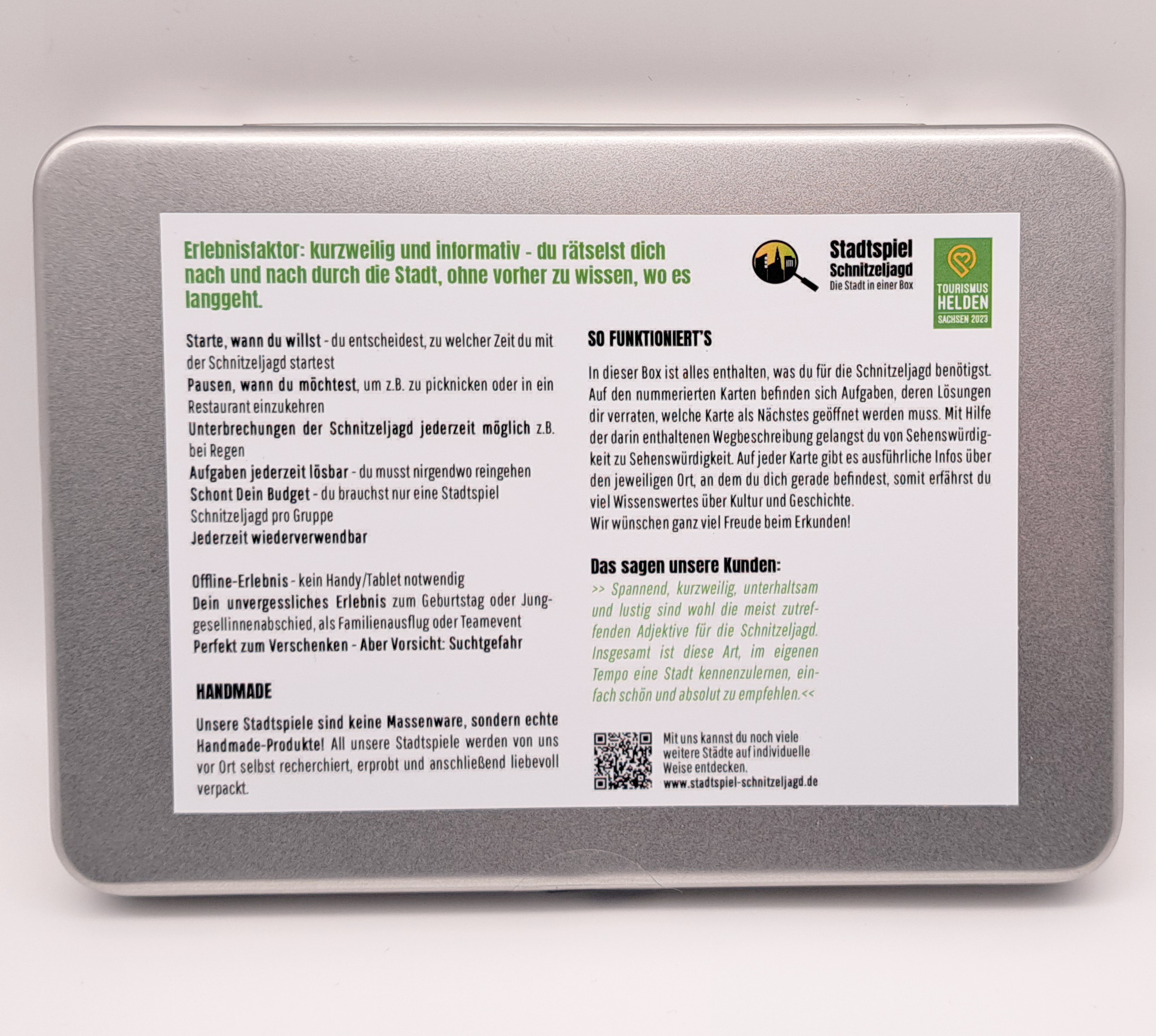 Auf der Rückseite ist auf der Metalbox ein Aufkleber mit weißem Hintergrund und daruf wird in grüner und schwarzer Schrift das Spiel beschrieben.