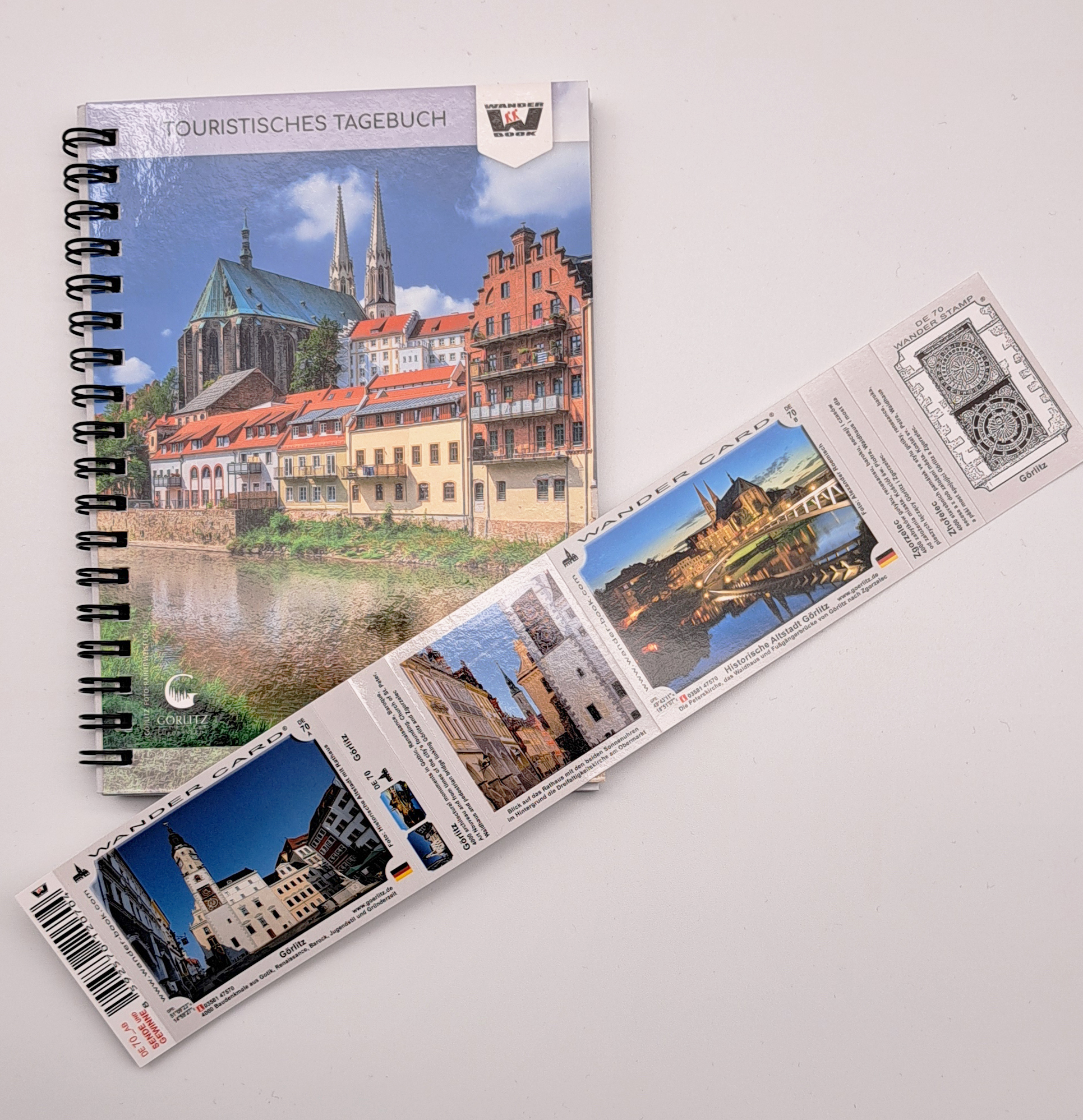 Das Wanderbook liegt auf einem weißen Untergrund. Auf der Titelseite ist die Neiße, die Häuserzeile auf der Deutschen Seite und die Kirche St. Peter und Paul zu sehen. Schräg darauf liegt die Doppelte Wander-Card, mit Motiven der Historischen Altstadt.