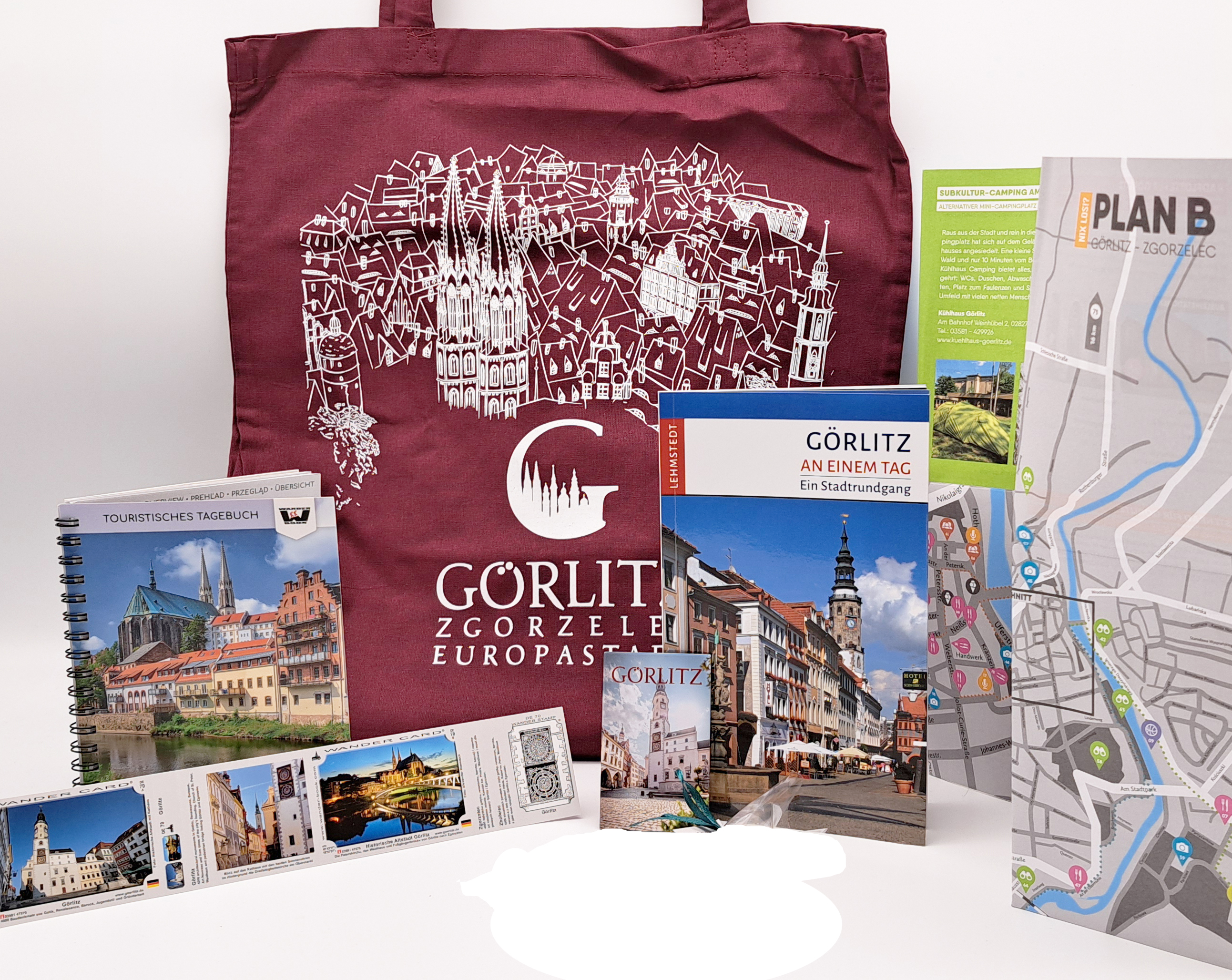 von links nach rechts sieht man aufgestellt: den Wander Card Aufkleber mit den Motiven Untermarkt und Altstadtbrücke mit Blick auf die Peterskirche, das Wander Book mit Görlitz Titelbild, den roten Stoffbeutel mit Görlitz Logo und Stadtshillouette, ein Ma
