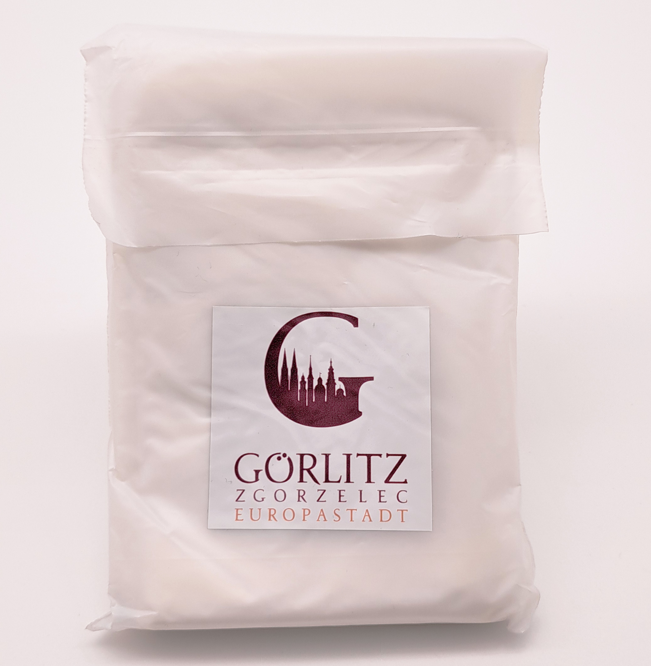 Verpackung des Regenponchos  von vorne auf der weißen aber doch etwas transparenten Verpackung vom Regenponcho ist ein Aufkleber mit weißem Hintergrund, auf dem das rote G mit der Shillouette der Görlitzer Türme. Darunter steht Görlitz Zgorzelec Europastadt.
