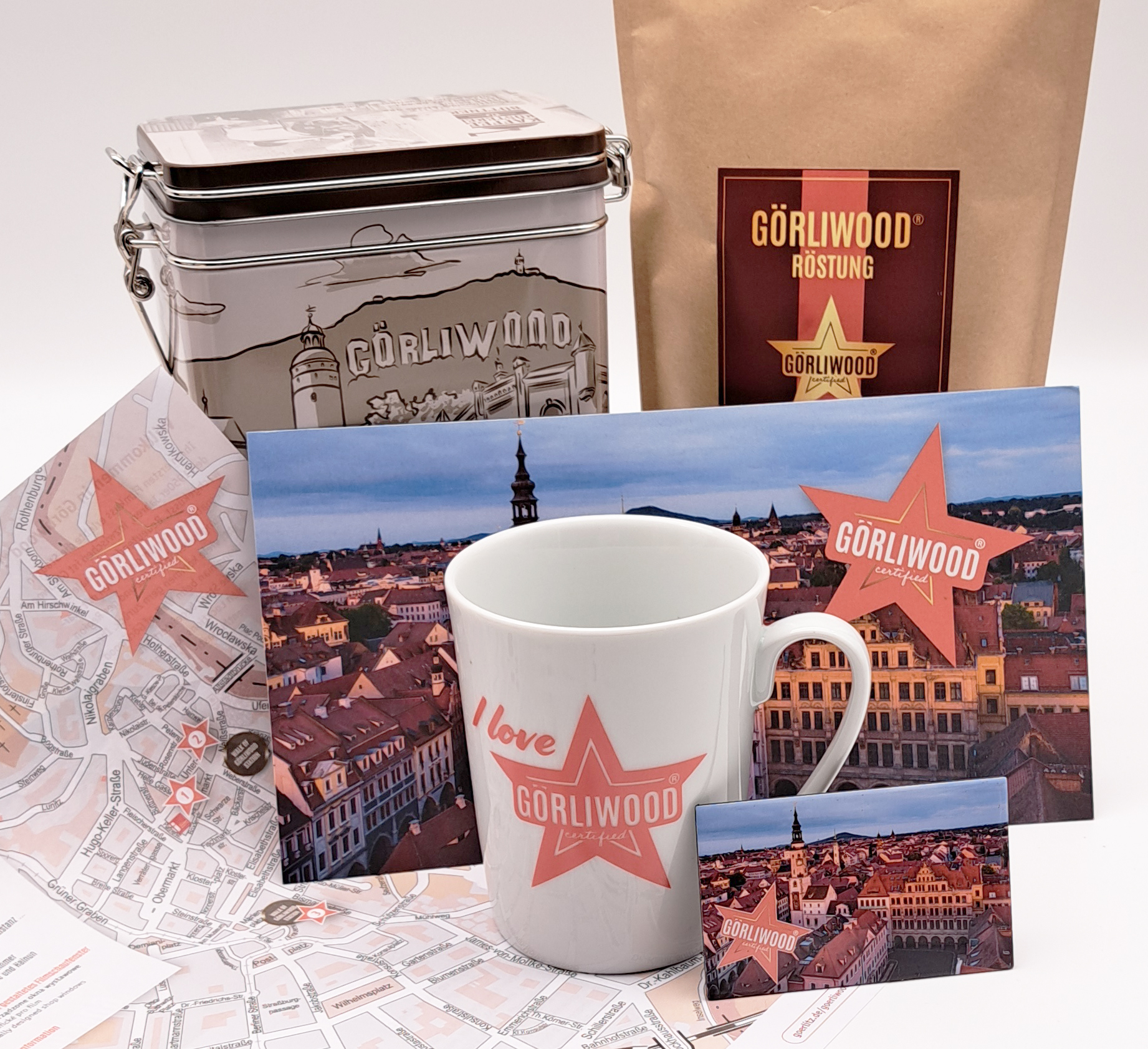 Alle Produkte, die zu diesem Set gehören sind abgebildet. Ganz vorne sieht man die Tasse mit dem Görliwood Stern, daneben ist noch der Görliwood-Magnet. Dann ist der Görliwood-Stadtplan und die Görliwood Postkarte zu erkennen. Dahinter ist die Kaffeedose 