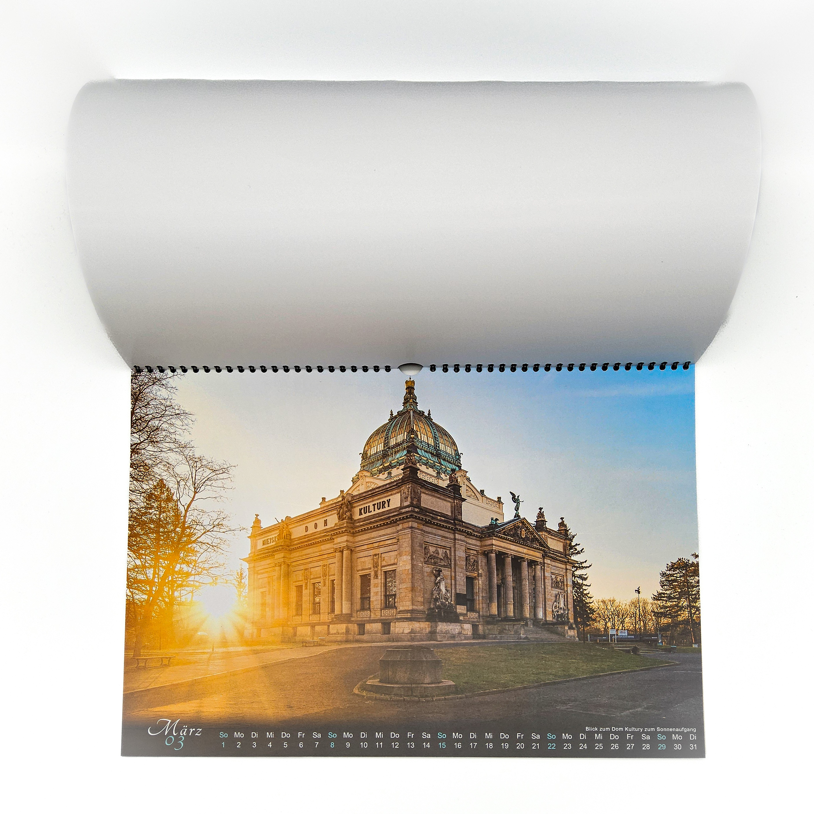Der Kalender Görlitz Rund um die Uhr ist aufgeblättert. Sie sehen die März-Ansicht mit dem Dom Kultury bei Sonnenaufgang