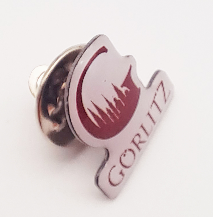 Der Pin ist von oben fotografiert. Man erkennt das Motiv von vorne aber auch den Anstecker, der an der Nadel steckt.