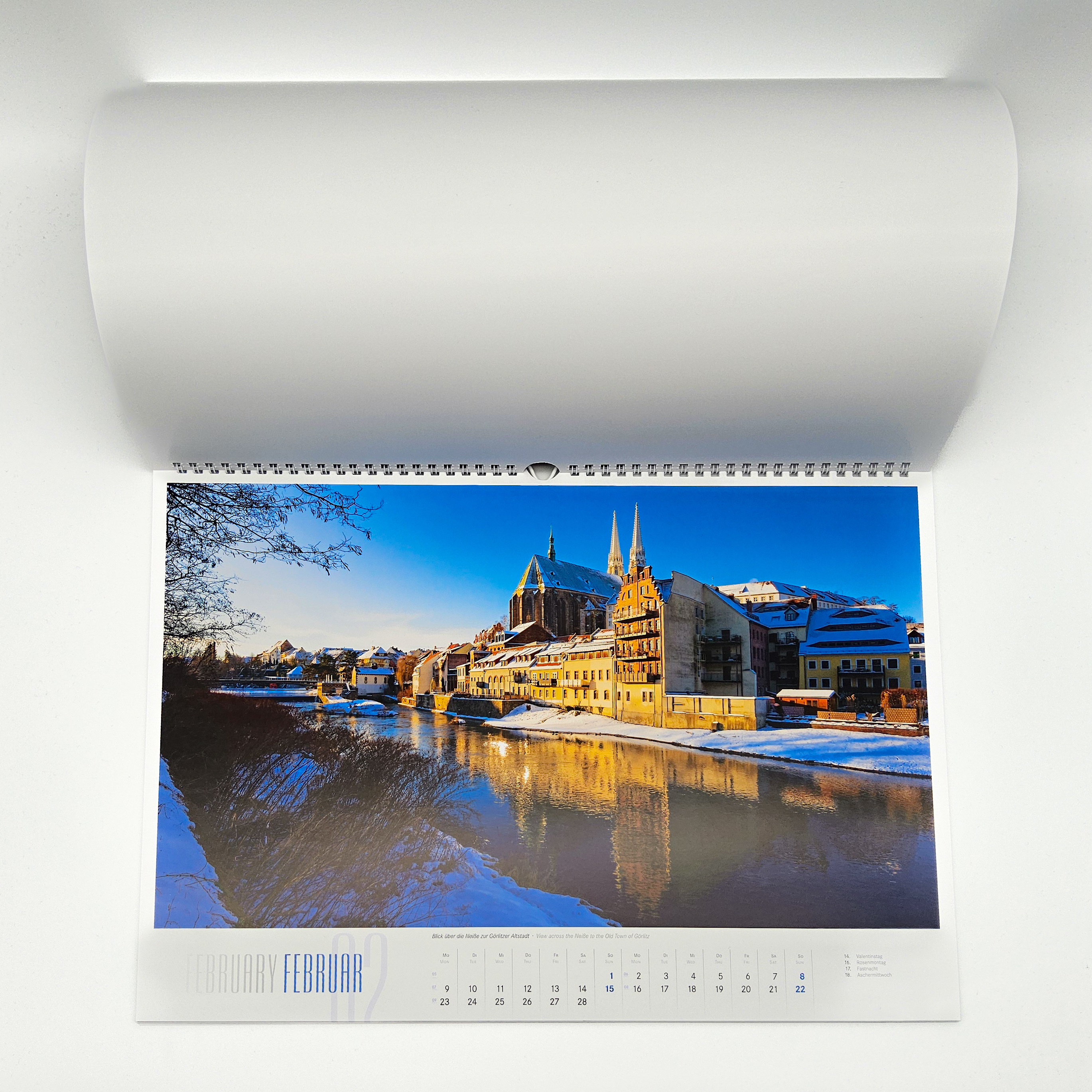 Der Kalender ist aufgeschlagen. Man sieht den Monat Februar. Auf dem Motiv ist die Kirche St. Peter und Paul zu sehen. Im Vordergrund ist die Neiße. Durch den Schnee entsteht eine winterliche Stimmung.