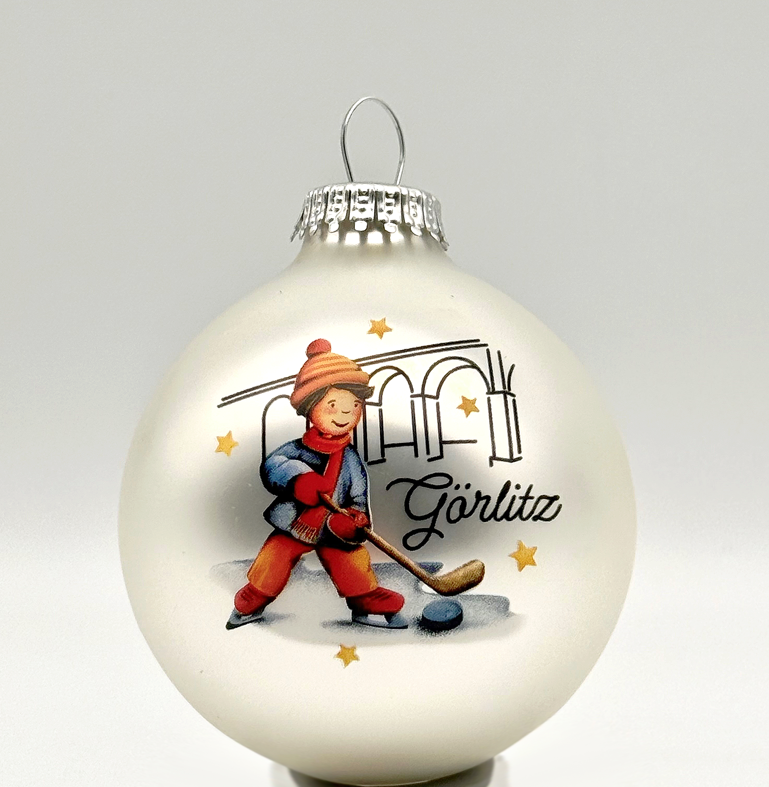 Die Weihnachtsbaumkugel 2025 ist silber-weiß und hat eine Zeichnung von einem Jungen beim Hockeyspielen als Hauptmotiv. Im Hintergrund ist der Viadukt abgebildet. Görlitz steht in geschwungener Schrift ebenfalls auf der Kugel.