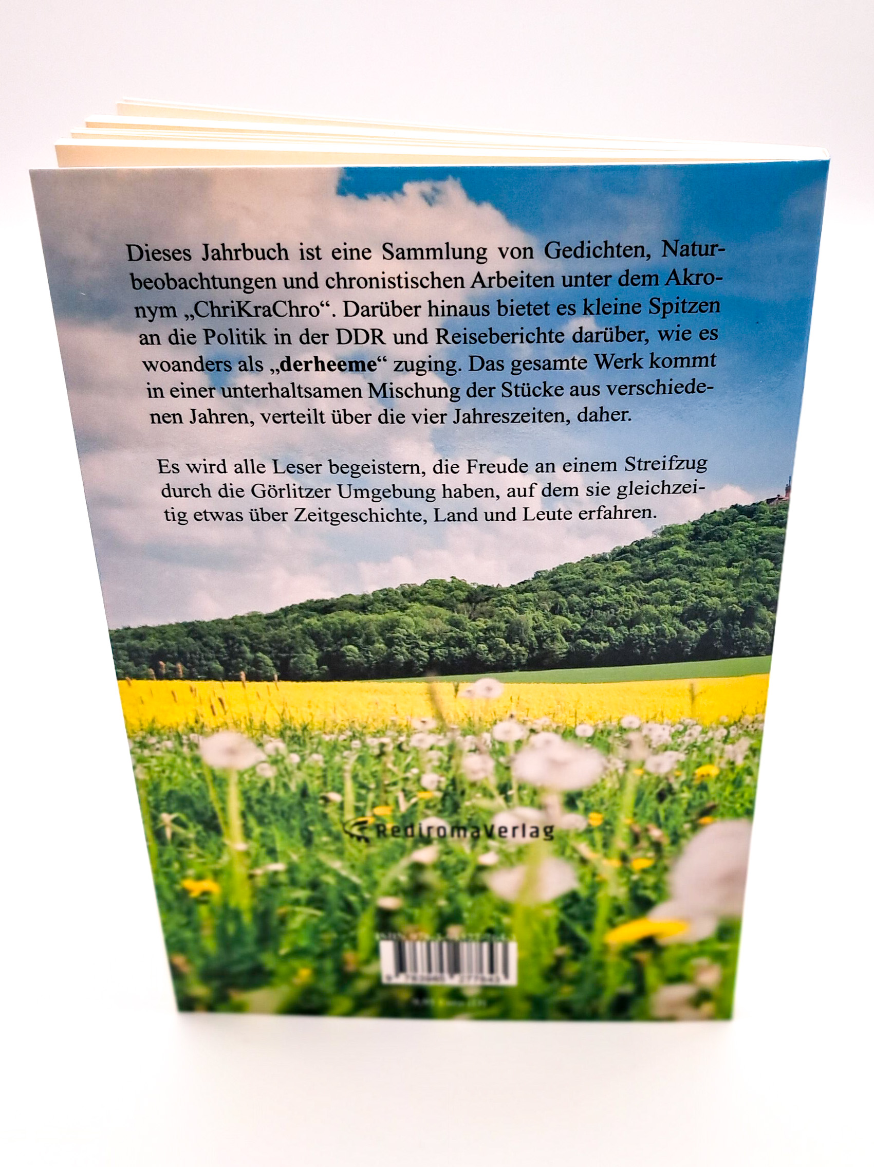 Auf der Rückseite ist im Vordergrund die Blumenwiese zu sehen, die vor der Landeskrone blüht. Am blauen Himmel sind ein paar Wolken zu sehen und über diesem Himmel ist in schwarzer Schrift die Buchbeschreibung zu lesen
